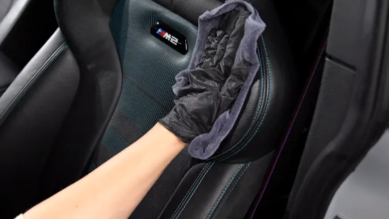 Gloved hand cleaning a leather seat with a purple cloth