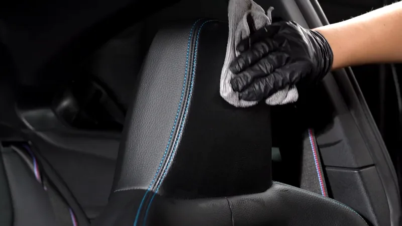 Gloved hand wiping excess coating from a leather headrest with a grey towel