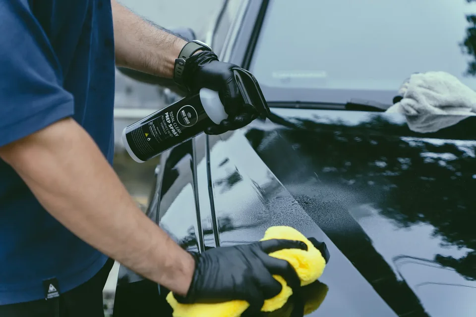 Detailer wiping a vehicle hood with a microfiber towel during surface preparation