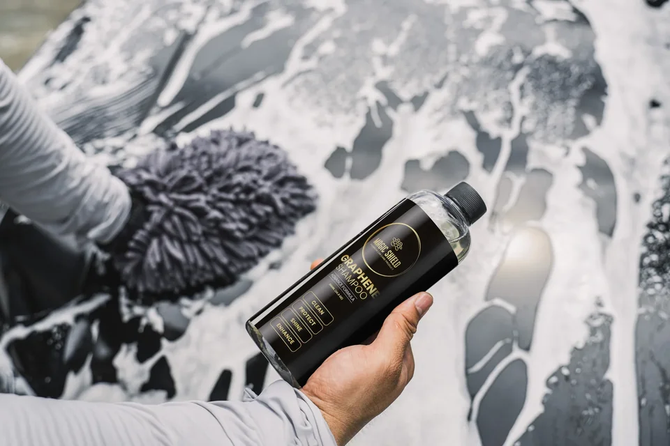 A 500 mL bottle of Graphene Shampoo held beside a wash mitt on a foamy car hood