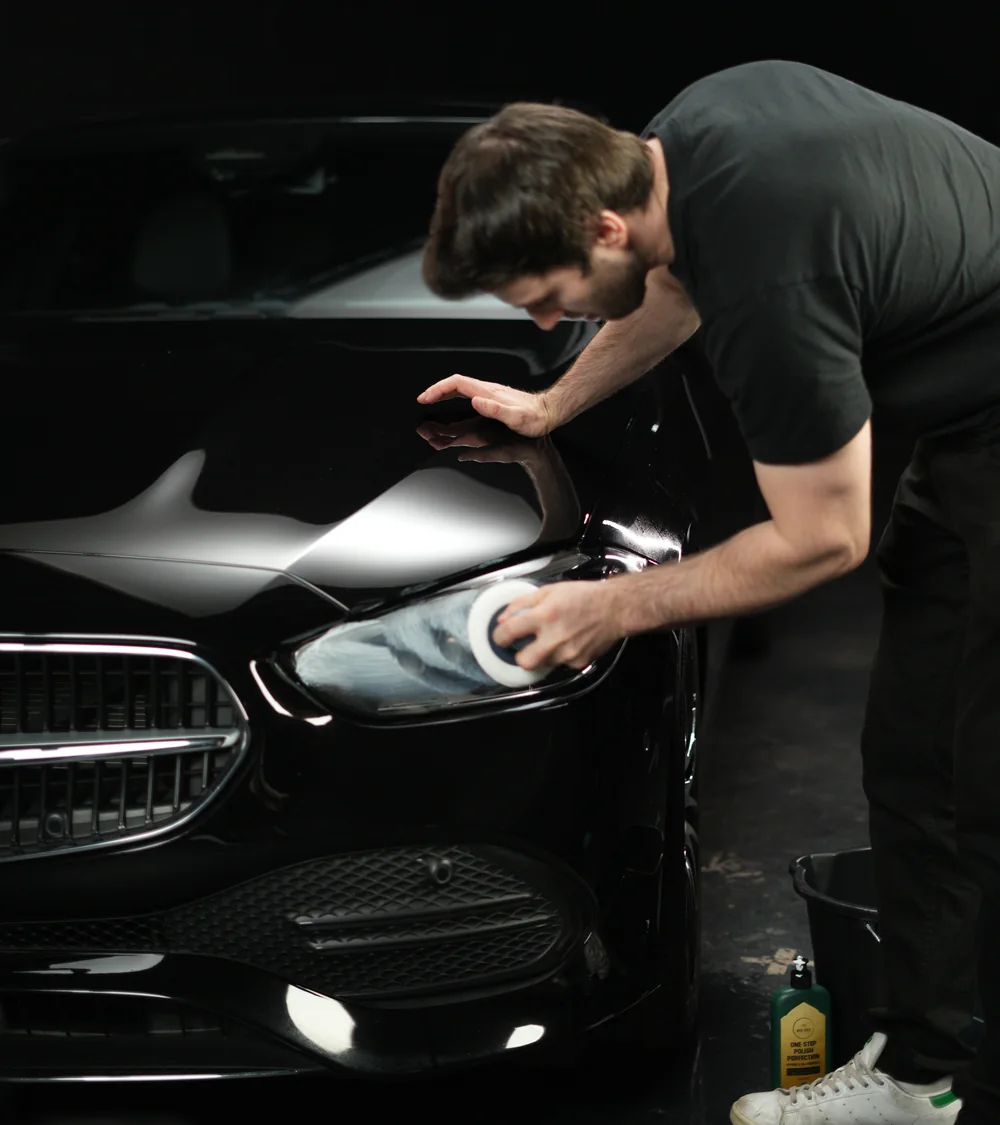 A man polishing the headlight of a black Mercedes