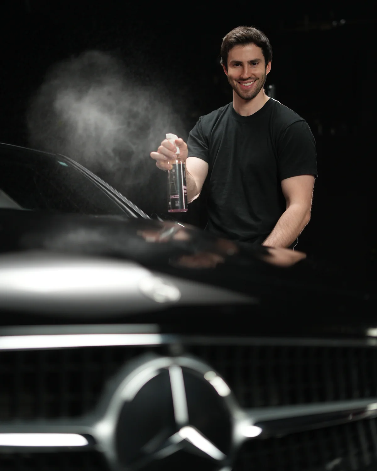 A smiling man caring for a black Mercedes in a detailing studio